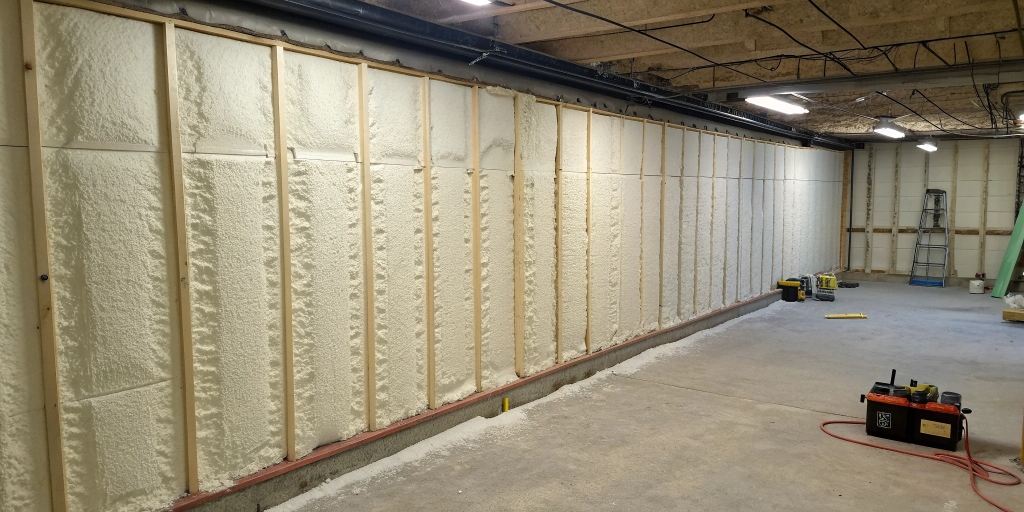Closed-cell spray foam in basement: Dense closed-cell spray foam insulates a basement wall, preventing moisture and improving thermal resistance.